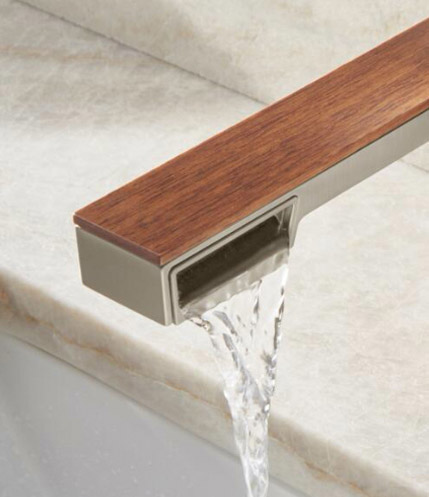 A close-up of the Single Handle Wall-Mount Lav from the Frank Lloyd Wright® Bath Collection by Brizo®, mounted above a marble sink. The water flow is turned on and pouring from the right side of the faucet.